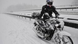 ein-mann-schiebt-sein-schneebedecktes-motorrad-bei-heftigem-schneetreiben-am-rand-der-autobahn-e19-bei-kontich-belgien-entlang.jpg